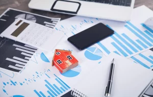 Materiais de marketing e finanças sobre uma mesa, com miniatura de casa e gráficos, representando estratégias de conteúdo para lançamento imobiliário.