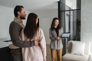 Profissional do setor imobiliário apresenta planta de imóvel a clientes durante reunião, ilustrando situações de objeções em vendas.